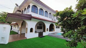 Ein zweistöckiges Haus mit überdachter Terrasse und Schwimmbecken.