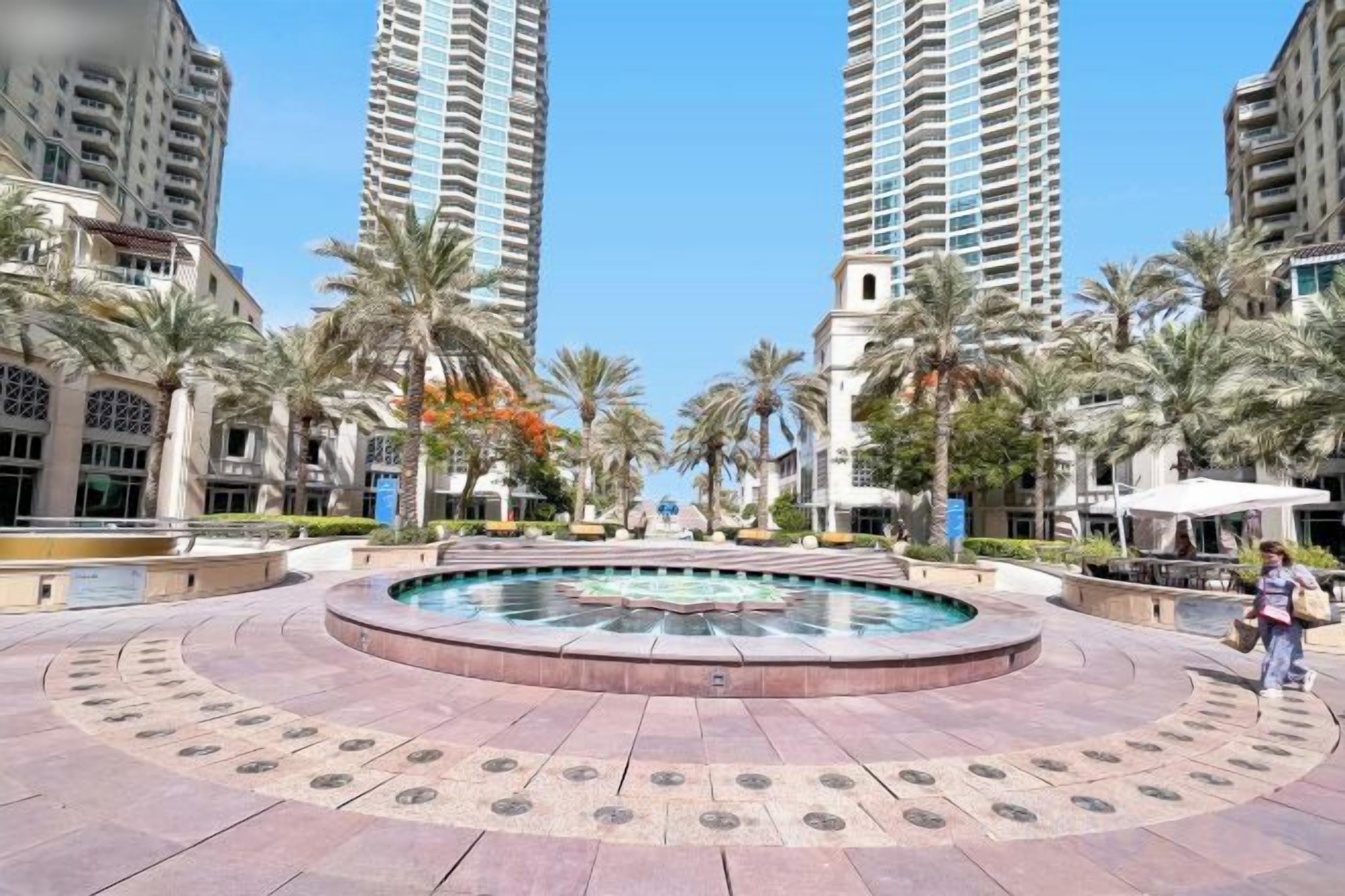 A courtyard with a central pool, surrounded by palm trees and high-rise buildings.