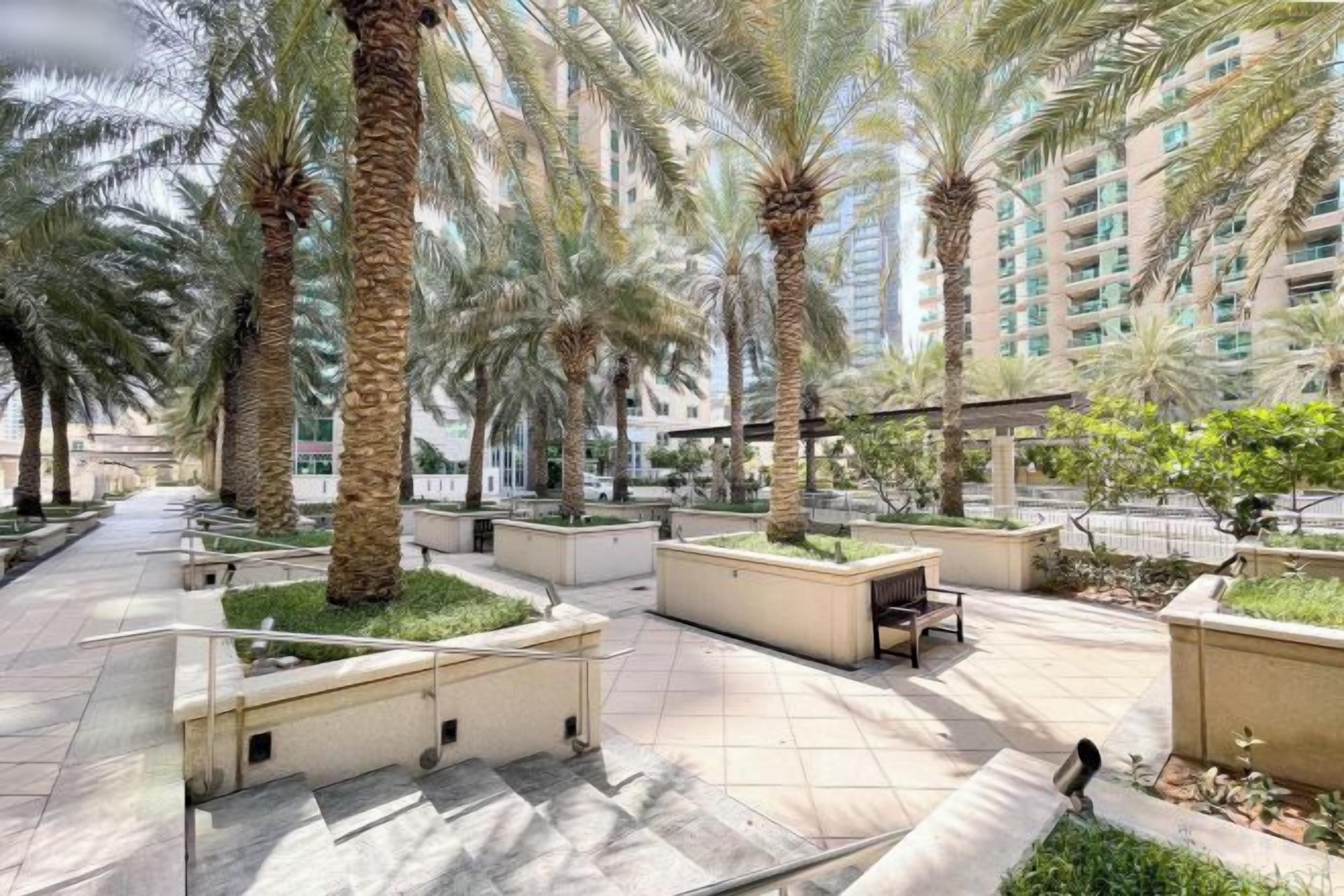 A courtyard with palm trees, outdoor seating, and a pathway leading to a building.