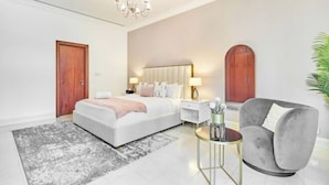 A modern bedroom with a large bed, bedside tables, a grey sofa, and a chandelier.