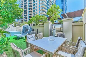 An outdoor patio with a table and chairs, a pool, and a view of high-rise buildings. - bnbme Dubai Marina: Quiet Patio Oasis (Dubai)