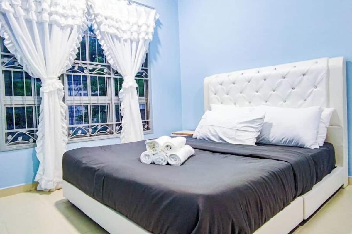A neatly made bed with a dark bedspread and white pillows, a white headboard, and a window with white curtains.