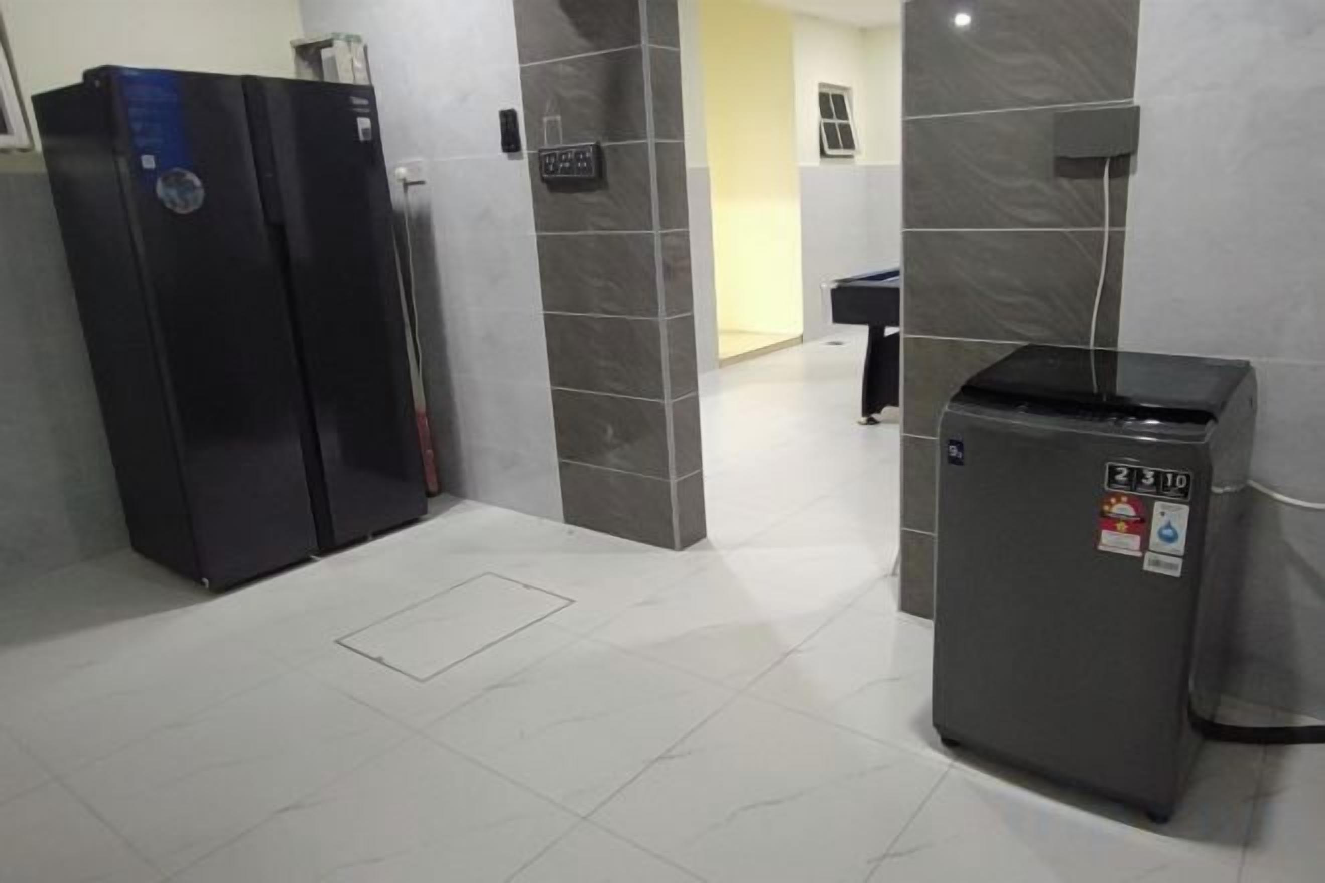 A hallway with a refrigerator, a trash bin, and a door leading to another room.