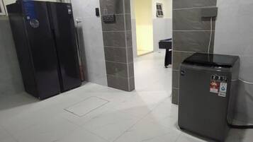A hallway with a refrigerator, a trash bin, and a door leading to another room.