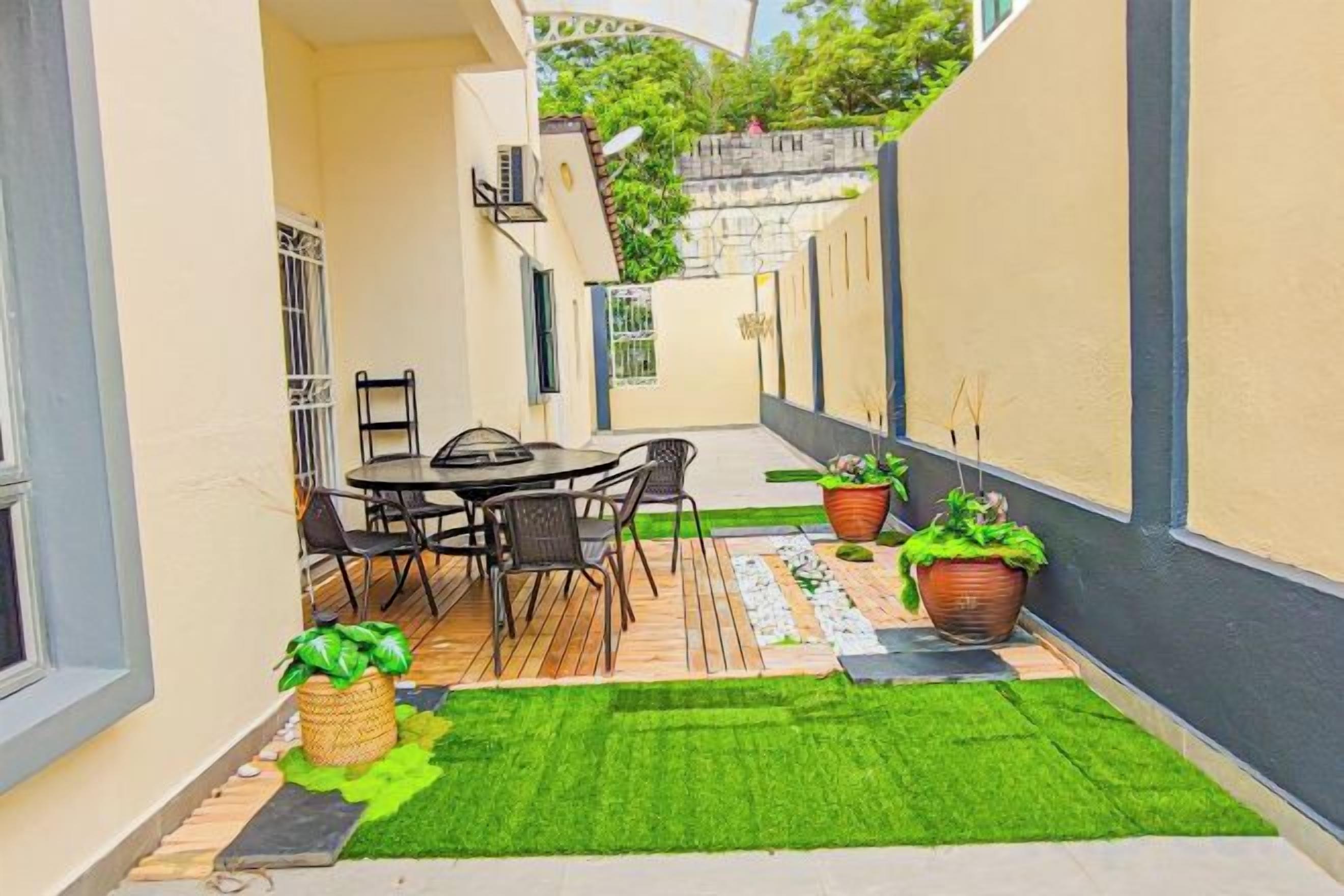 A patio with a table and chairs, a small garden area with potted plants, and a green artificial turf.