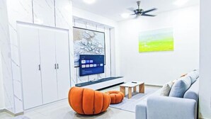 A modern living room with a grey sofa, orange ottoman, and a flat-screen TV on a stand. - Modern 5-Bedroom House BBQ Event Wedding at Kajang by HCK (Kajang)
