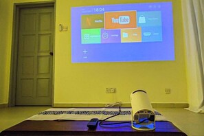 A projection screen displaying a YouTube interface on a wall, a remote control, and a speaker on a table. - Modern 5-Bedroom House BBQ Event Wedding at Kajang by HCK (Kajang)