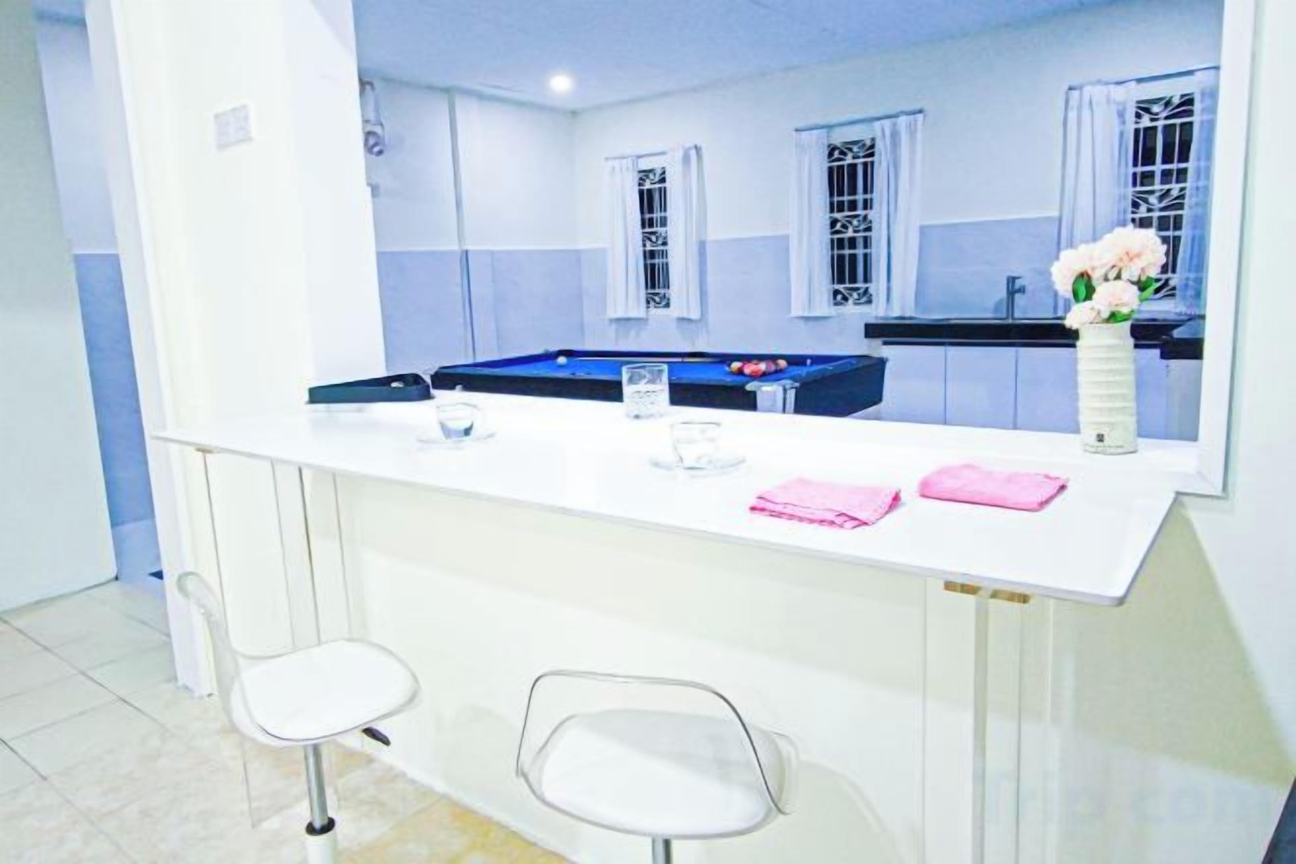 Habitación con barra blanca, dos taburetes, mesa de billar y ventana con vistas.