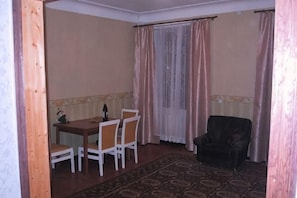 A dining area with a table and chairs, a patterned rug, and a window with curtains.