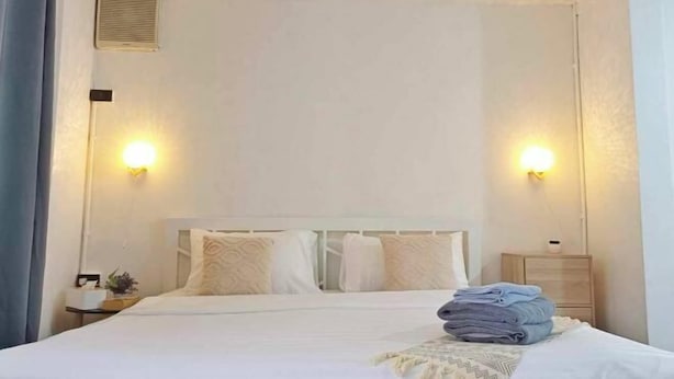 Una cama bien hecha con una toalla doblada y una mesita de noche con una lámpara.