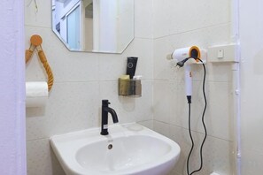 Un baño con lavamanos blanco, un espejo, un secador de pelo y artículos de aseo.