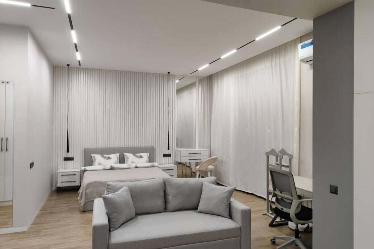 A modern bedroom with a bed, bedside tables, a desk, and a chair.