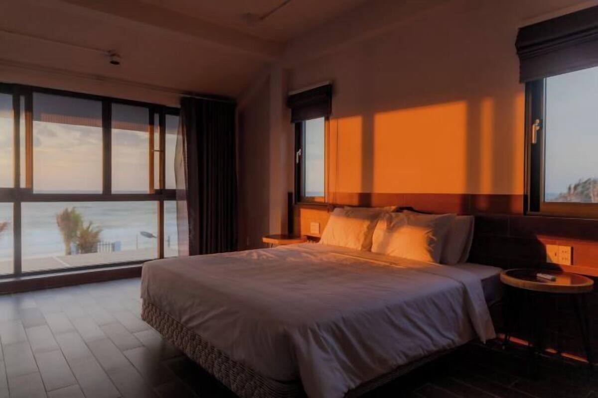 A bedroom with a large bed, a nightstand, and a view through a window.