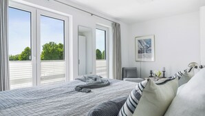 A bedroom with a large bed, a chair, a desk, and a window with curtains. - Vacation home Bellevue directly on the Schlei with fireplace, sauna and whirlpool (Kappeln)
