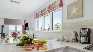 A modern kitchen with a large window, a wooden star wall decoration, and a variety of fresh vegetables on the counter. - Vacation home Bellevue directly on the Schlei with fireplace, sauna and whirlpool (Kappeln)