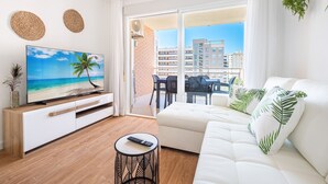 Una sala de estar moderna con un televisor de pantalla plana, un sofá blanco y un balcón con vistas a edificios.