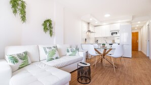 Una sala de estar moderna con un sofá blanco, una mesa de comedor con sillas y una cocina al fondo.