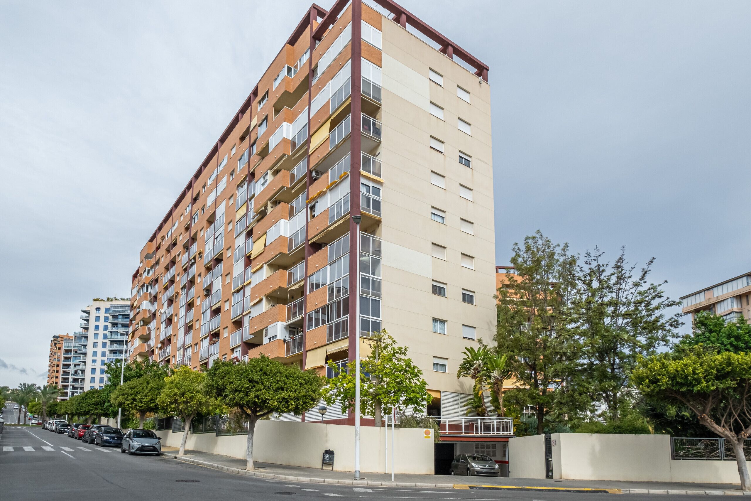 A multi-story residential building with balconies, a parking area, and a street view.