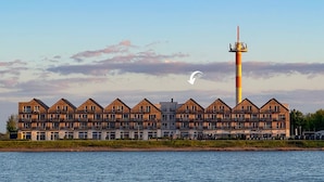 A waterfront hotel with a row of wooden-framed buildings, a tall tower, and a view of the water. - Vacation apartment Moby Dick OstseeResort Olpenitz - sea view, balcony & harbor flair (Kappeln)
