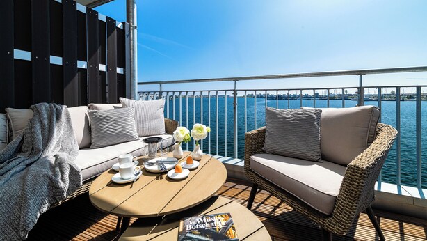 Een balkon met een bank, een tafel en uitzicht op het water.