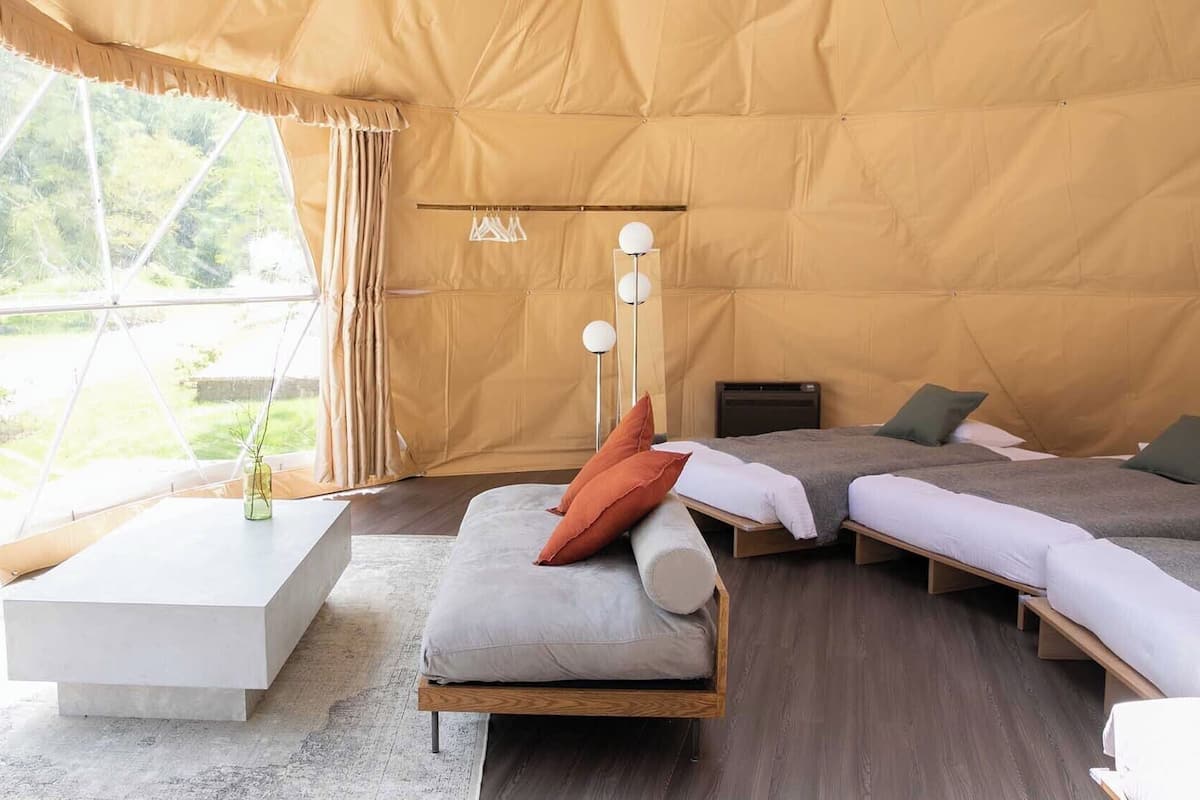 A tent-style room with two beds, a sofa, a coffee table, and a lamp.