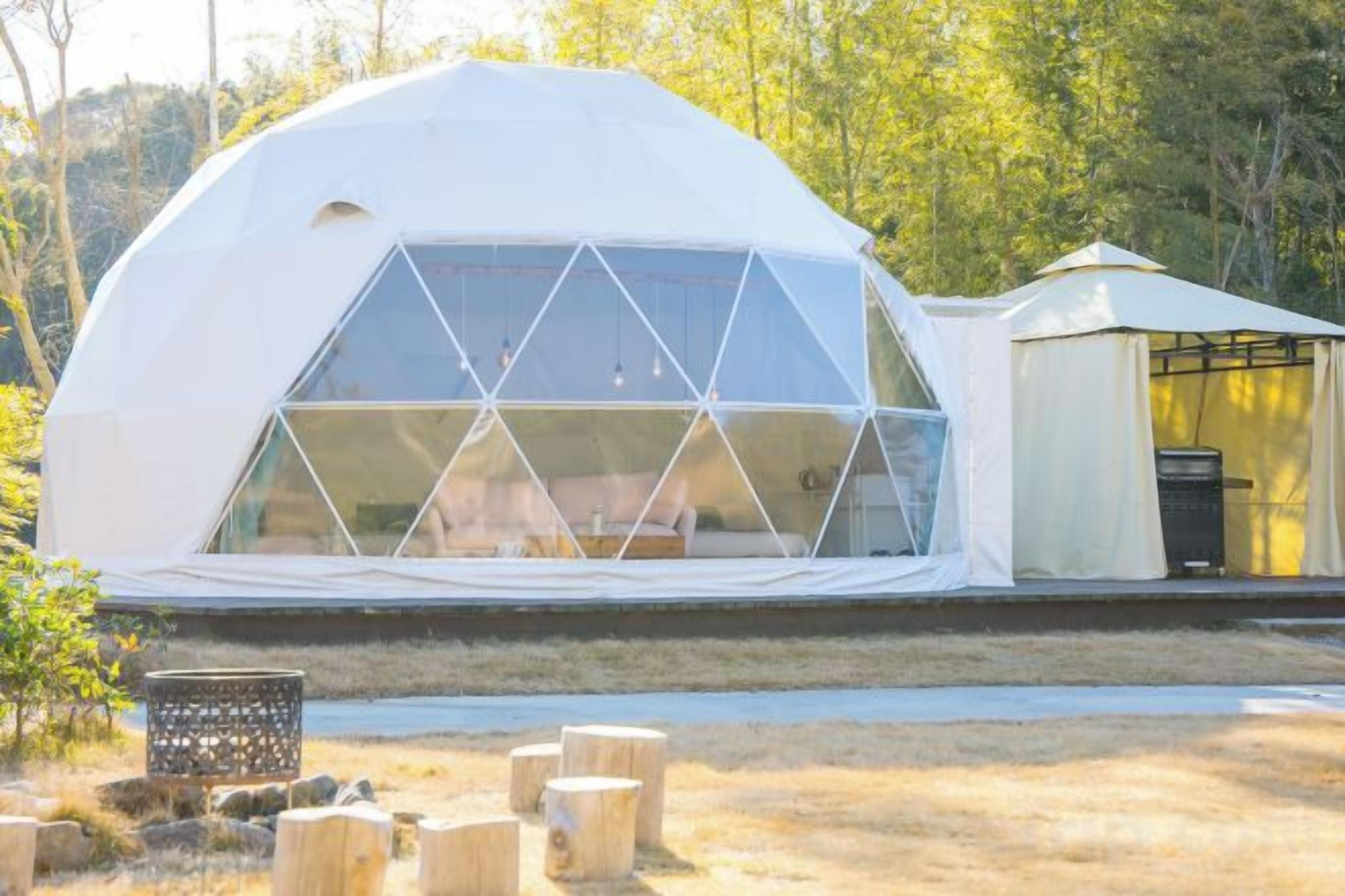 A geodesic dome structure with a glass facade, a small attached structure, and a fire pit in the foreground.