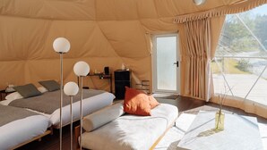 A tent-style room with two beds, a sofa, a small table, and a window with curtains.