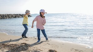 Two people walking on a sandy beach with a rocky shoreline in the background.