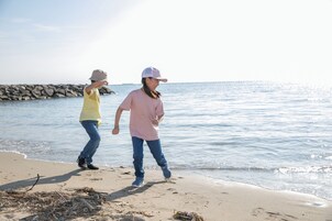 Dos personas caminando sobre una playa arenosa con una costa rocosa al fondo.