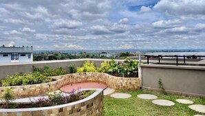 A rooftop garden with a curved stone planter, a circular seating area, and a view of the cityscape. - Modern 1Br, Queen, Gym, Pool,Central in Kileleshwa (Nairobi)