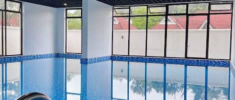 An indoor swimming pool with clear blue water, large windows, and a modern ceiling design.