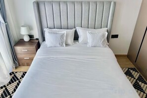 A hotel room with a large bed, a bedside table with a lamp, and a patterned rug. - Modern 1Br, Queen, Gym, Pool,Central in Kileleshwa (Nairobi)