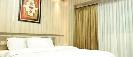 A hotel room with a bed, a framed artwork on the wall, and a window with curtains.
