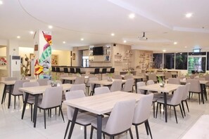 A modern dining area with multiple tables and chairs, a kitchen in the background, and a large decorative column. - Graha Sumsel Jakarta (Central Jakarta)