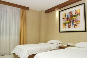 A hotel room with two beds, a framed artwork on the wall, a telephone on the nightstand, and a window with curtains.