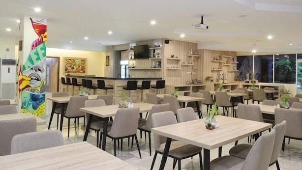 A modern dining area with multiple tables and chairs, a kitchen in the background, and a large window providing natural light. - Graha Sumsel Jakarta (Central Jakarta)