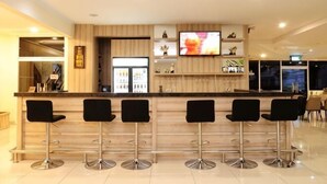 A bar area with a wooden counter, black bar stools, a television screen, and a refrigerator. - Graha Sumsel Jakarta (Central Jakarta)