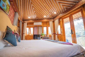 Un dormitorio con cama, televisión, escritorio con planta y ventanas amplias.