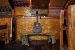 A wooden interior with a guitar leaning against a wall, a bench, and patterned wall decorations. - Sinai Bungalow & Hotel SaPa (Sapa)