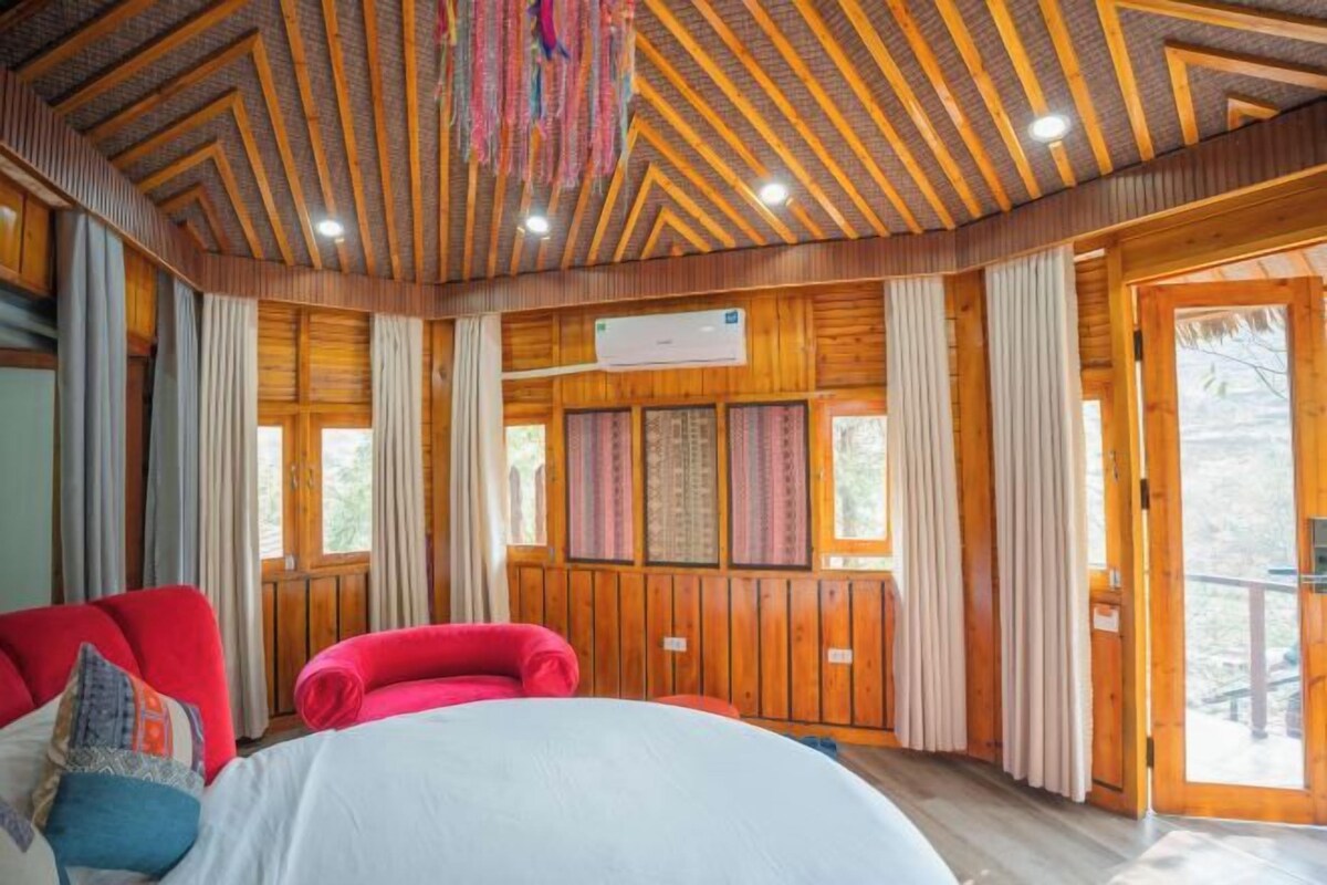 Una cabaña de madera con una cama, un sillón rojo y un ventanal con cortinas.