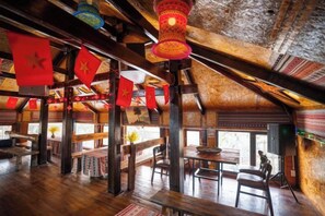 An interior with wooden beams, tables, and chairs, and red flags hanging from the ceiling. - Sinai Bungalow & Hotel SaPa (Sapa)