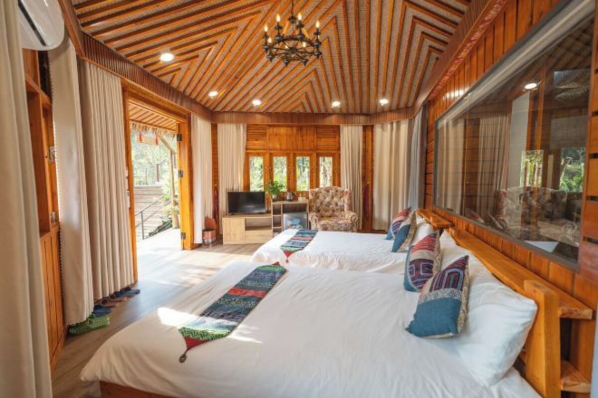 Una habitación con dos camas, techo de madera, ventanas amplias y un televisor.