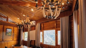 Un salón de conferencias con una mesa larga y sillas, paneles de madera y un gran ventanal con vistas a árboles.