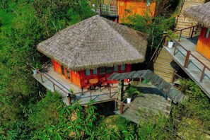 A thatched-roof bungalow with a wooden deck and outdoor seating area, surrounded by lush greenery. - Sinai Bungalow & Hotel SaPa (Sapa)