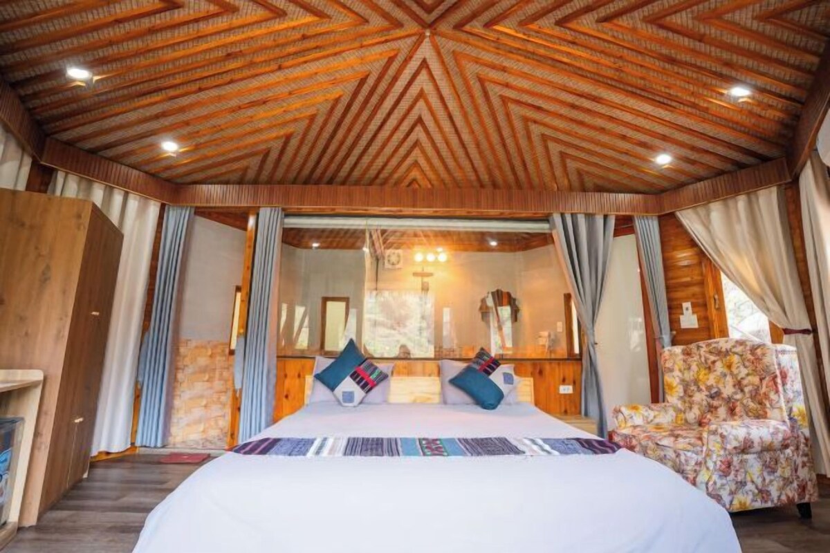 Una habitación con techo de madera, una cama con almohadas, una silla y cortinas.