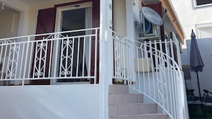 A single-story house with a covered porch, a satellite dish, and a small outdoor seating area. - House located 100 meters from one of the Caribbean's most beautiful beaches (Sainte-Anne)
