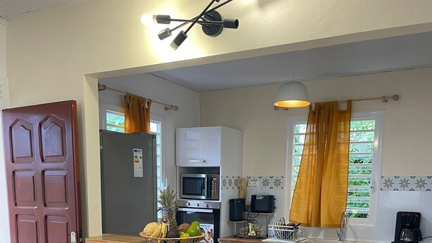 A compact kitchen with a central island, two bar stools, a microwave, a coffee maker, and a refrigerator. - House located 100 meters from one of the Caribbean's most beautiful beaches (Sainte-Anne)