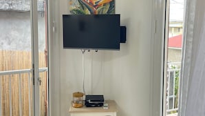 A room with a flat-screen TV mounted on the wall, a small table with a coffee maker, and a basket underneath. - House located 100 meters from one of the Caribbean's most beautiful beaches (Sainte-Anne)