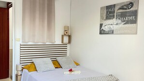 A neatly arranged bedroom with a bed, pillows, a bedside table, a wall-mounted lamp, and a decorative item. - House located 100 meters from one of the Caribbean's most beautiful beaches (Sainte-Anne)
