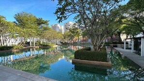 A serene outdoor pool area with a clear reflection, surrounded by greenery and modern buildings in the background. - Cozy Straits Quay Seafront Homestay (Tanjung Tokong)